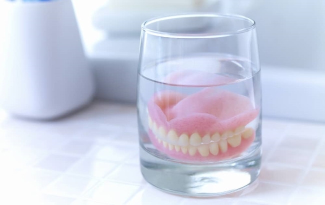 Soak dentures in white vinegar overnight and clean it with a toothbrush in the morning.