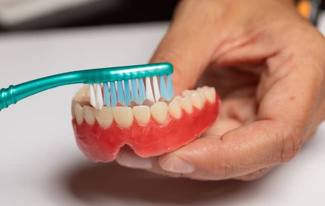 Clean your dentures daily with a soft toothbrush, water, and a denture specific cleaner.