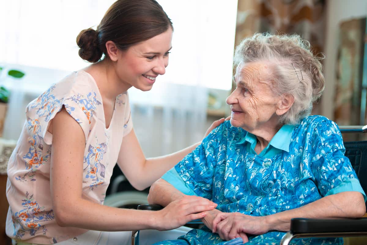 Smiling aged care resident receiving support from a carer during a mobile dental visit.