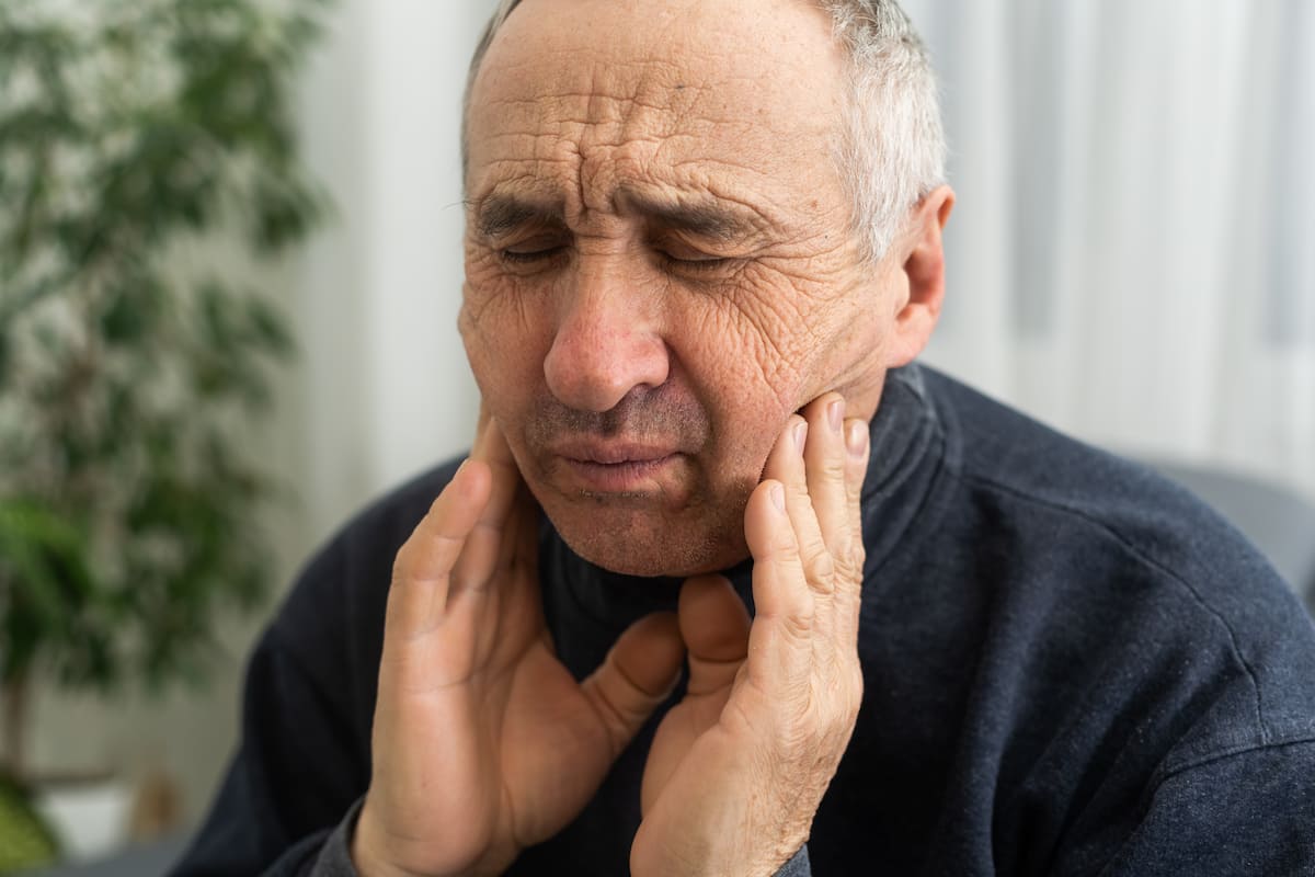 Older man holding his jaw in pain from clenching and grinding teeth.