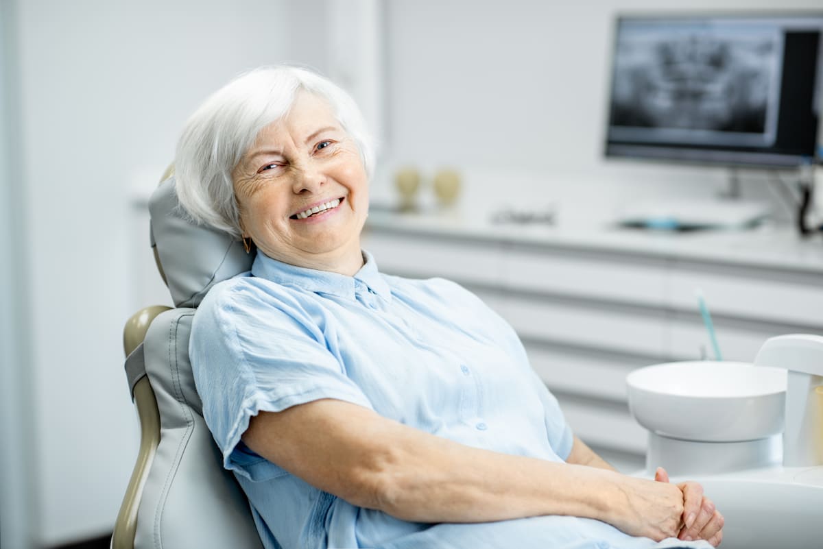 Smiling elderly woman in dental chair after successful muscle relaxant treatment for jaw clenching.