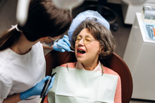 Senior woman receiving mobile teeth cleaning treatment from a dental professional in a Perth home.