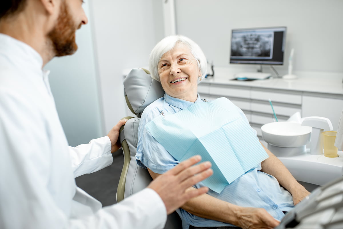 Smiling elderly woman speaking with a dentist before receiving IV sedation treatment.