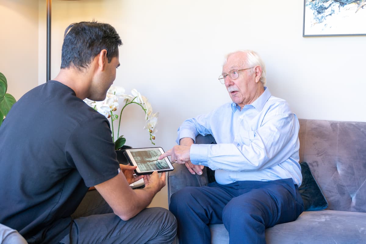 Elderly man discussing dental X-ray with a dentist during an in-home consultation.