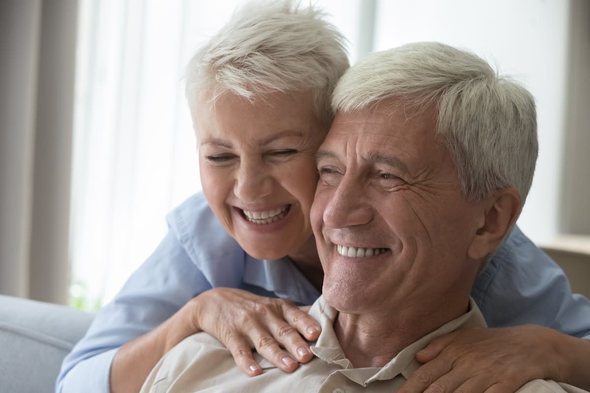 Smiling older couple embracing at home, showing confidence and happiness with new dentures.