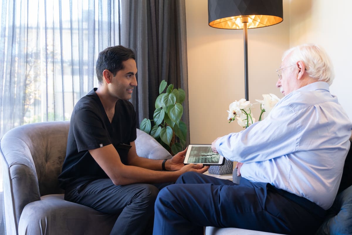 Dentist showing an elderly patient a dental scan on a tablet during a consultation.