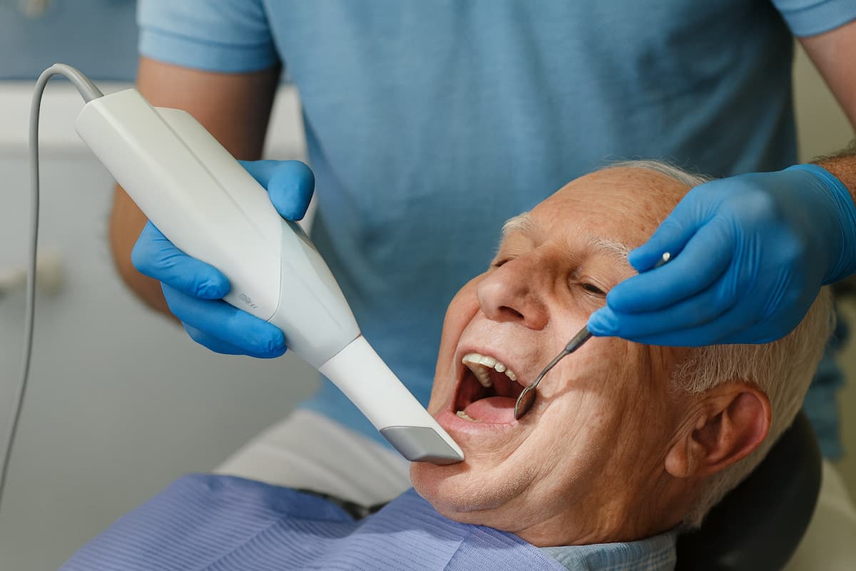 Dentist using an intra oral scanner on an elderly man during a dental appointment.