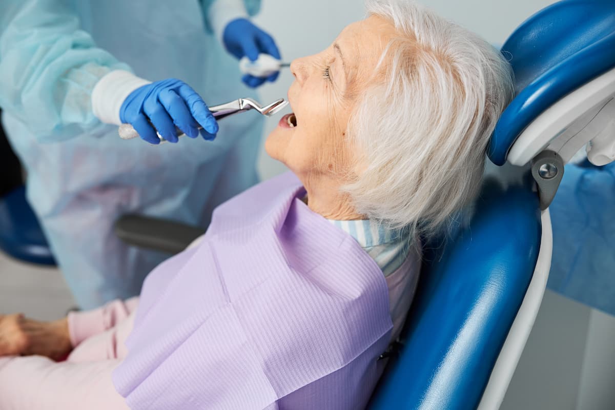 Elderly woman receiving a tooth extraction from a dentist wearing protective gloves in a dental clinic.