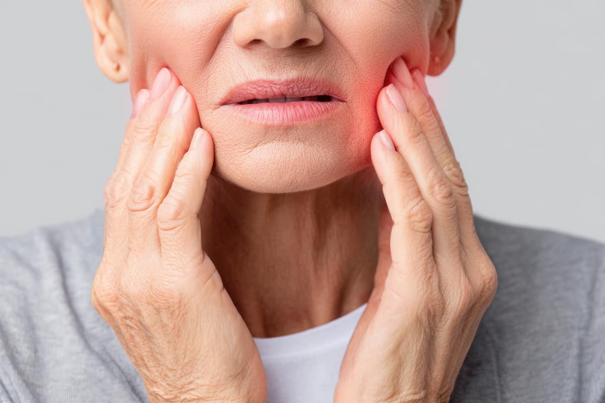 Elderly woman holding her jaw due to dental pain and possible tooth decay.