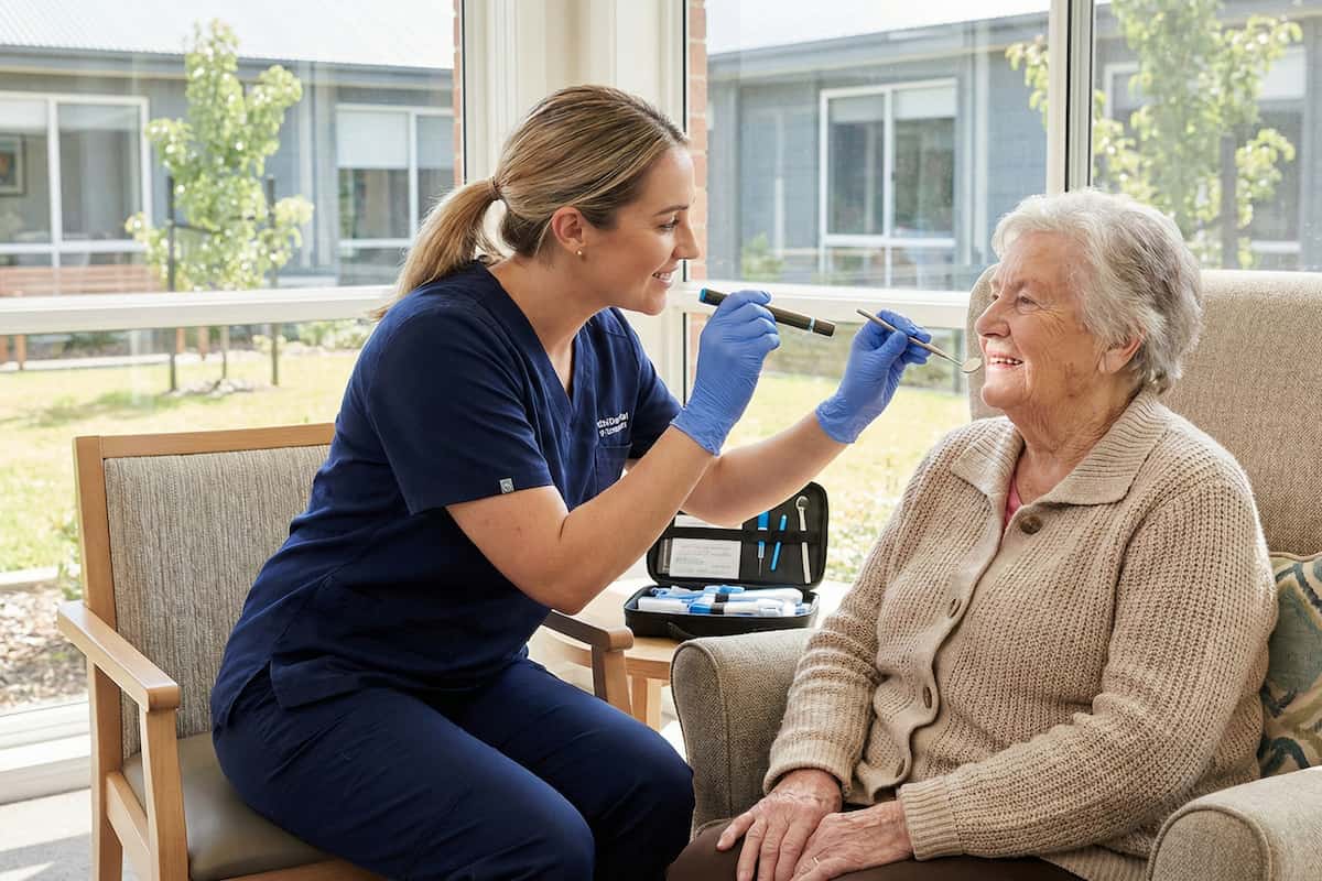 Dental professional performing a gentle in-home oral health assessment for an aged care resident in a familiar, comfortable setting.